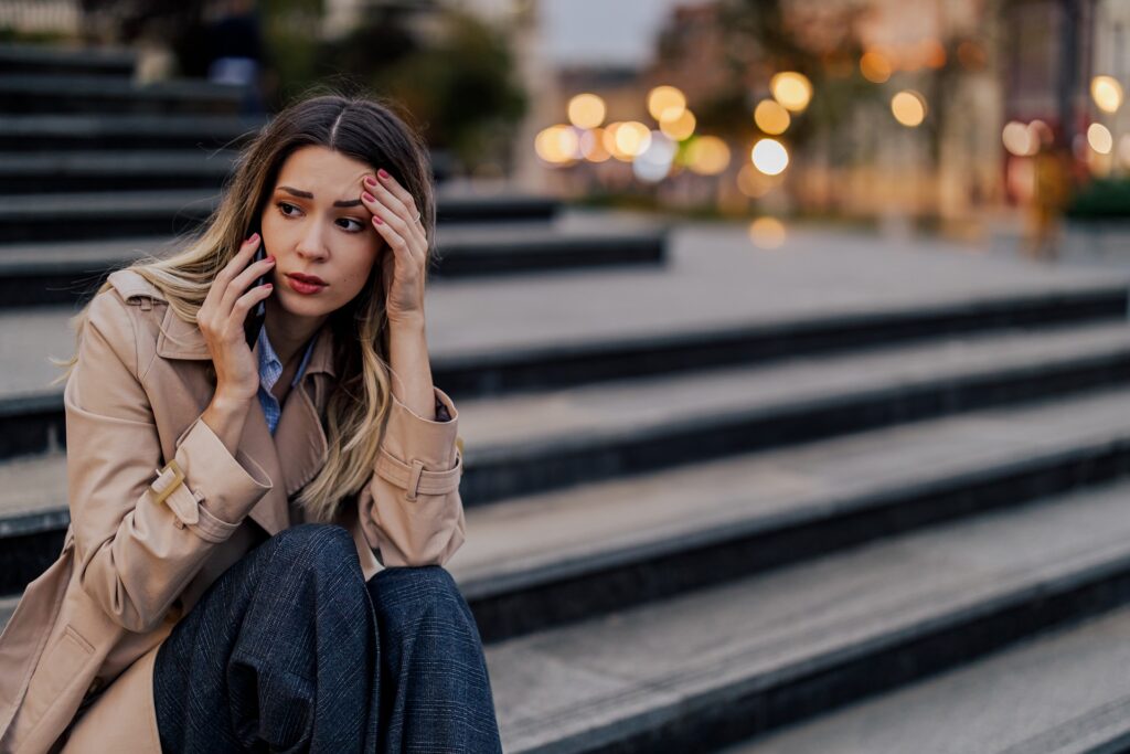 Sad woman sitting on a stairs in a city street and talking on the phone.